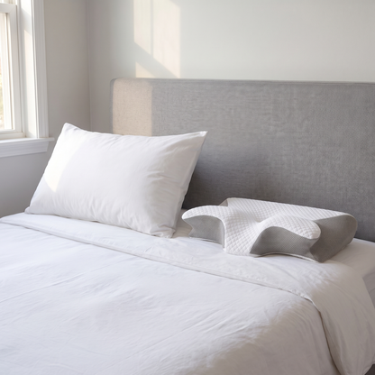 NeckRest nekkussen naast een gewoon hoofdkussen op bed, waardoor je ziet dat het NeckRest een stuk compacter is